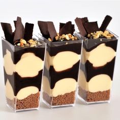 three desserts with chocolate, nuts and cream in small containers on a white surface