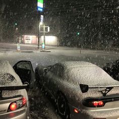 two cars are parked in the snow at a gas station, one is covered with snow