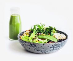 a bowl of salad next to a bottle of green juice