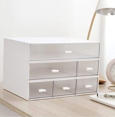 a white box sitting on top of a wooden desk next to a clock and lamp