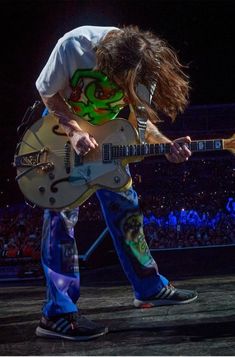 a man with long hair playing an electric guitar in front of a large audience at a concert