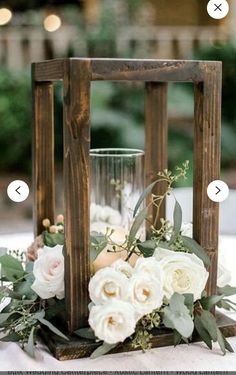 a wooden lantern with flowers and greenery in it is sitting on a tablecloth