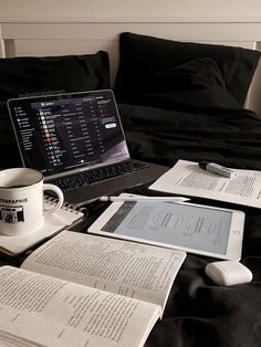 an open laptop computer sitting on top of a bed next to papers and a cup