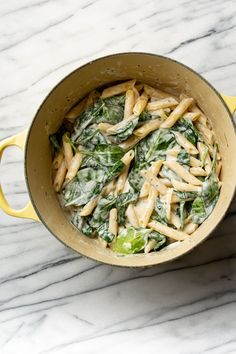 a pot filled with pasta and spinach on top of a marble counter