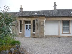 an old stone building with two doors and windows on the front, next to a gravel driveway