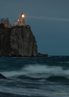 a light house on top of a rock in the ocean at night with waves crashing around it