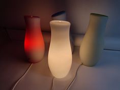 three different colored vases sitting next to each other on a table with a white cord