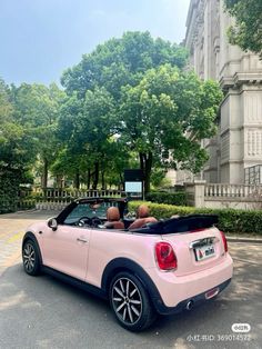 two people in a pink convertible car parked on the street next to a large building