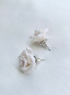 two white roses are sitting on top of some silver pins and studs that are attached to each other