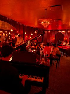 a group of people sitting around a piano in a room with red lighting and chandeliers