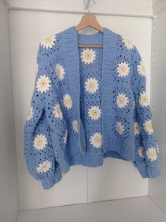 a blue sweater with white and yellow flowers is hanging on a hanger in a closet