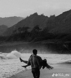 a man carrying a woman on his back while walking along the beach in black and white