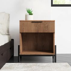 a nightstand with a potted plant on it next to a bed