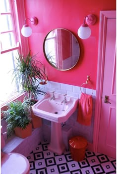 a bathroom with pink walls and black and white flooring, potted plants in the corner