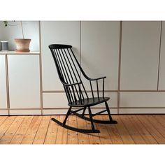 a black rocking chair sitting on top of a hard wood floor next to a white wall