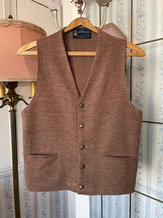 "This is a lightweight vest in medium brown, which up close also has hints of rusty brown, golden yellow and green. Made from \"Scampoli Double Knit by Tony Day,\" the vest has the original burnished gold metal buttons, two front pockets and is partially lined. Marked size medium. The measurements, taken with the vest lying flat, are: shoulder to shoulder, 12 inches; armpit to armpit, 19 inches; length, 23 inches; bottom edge, 19 inches. In very good condition." Fitted Brown Wool Cardigan, Fitted Brown Wool Vest, Brown Sleeveless Sweater Vest With Pockets, Brown V-neck Sweater Vest For Fall, Classic Brown Wool Sweater Vest, Fitted Brown Winter Vest, Sleeveless Brown Cardigan For Fall, Fitted Brown Sleeveless Sweater Vest, Brown V-neck Vest For Winter