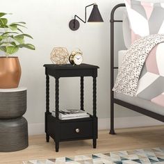 a small black end table next to a bed with a plant on it and a clock