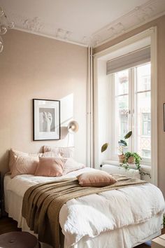 a white bed sitting next to a window in a bedroom under a framed picture on the wall