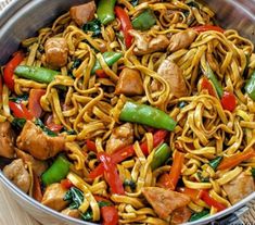 a pan filled with noodles, chicken and veggies on top of a wooden table