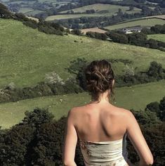 a woman standing on top of a lush green hillside next to a lush green field