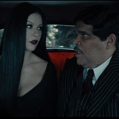 a man and woman sitting in the back seat of a car, one with long black hair