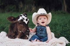 a baby wearing a cowboy hat sitting next to a cow on top of a blanket