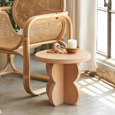 a wicker chair next to a small table with a candle on it in front of a window