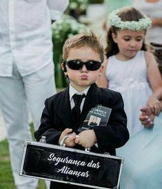 a little boy dressed in a tuxedo and sunglasses holding a sign that says saguaria des alunas