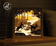 an illuminated card with deer running in the woods at sunset, on a table next to a glass of water