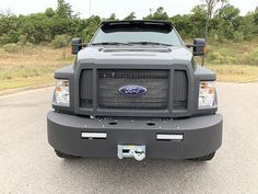 the front end of a gray truck parked in a parking lot next to some trees