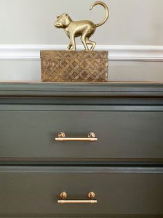 a gold dog figurine on top of a green dresser with brass handles and knobs