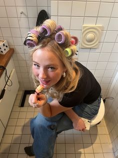 a girl with curlers on her head is brushing her teeth in the bathroom while holding a toothbrush