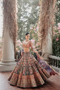 a woman standing in front of some flowers wearing a long dress with an intricate pattern on it