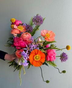 a person holding a bouquet of flowers in front of a white wall with purple, orange and pink flowers