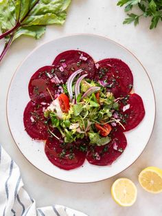 beet salad on a white plate with lemon wedges and parsley next to it