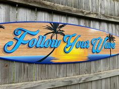 a wooden sign that says follow your wave on the side of a fence with palm trees