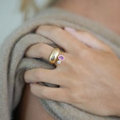 a woman's hand wearing a gold ring with two pink stones on the side