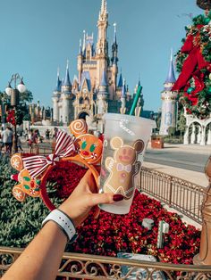 a person holding up a cup with mickey mouse on it in front of a castle