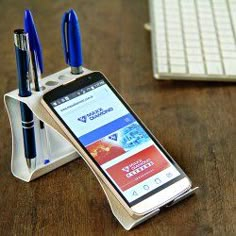 a cell phone sitting on top of a desk next to a pen holder with two pens