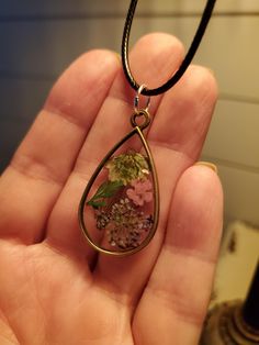 a hand holding a glass pendant with flowers in the center and green leaves on it