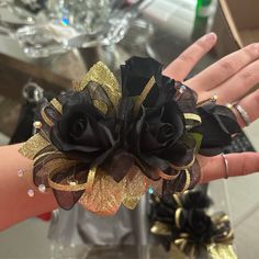 a woman's hand holding a black and gold wrist corsage