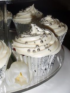 cupcakes with white frosting and silver decorations on a clear platter, ready to be eaten