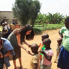 a woman handing something to children on a dirt road