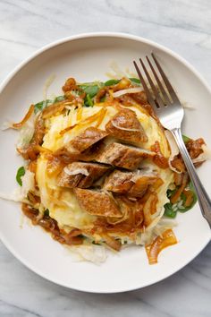 a white plate topped with meat and cheese covered in sauce next to a silver fork