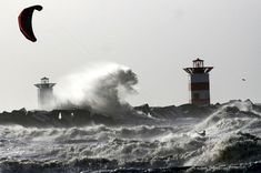 a person parasailing in the ocean next to a lighthouse with waves crashing against it