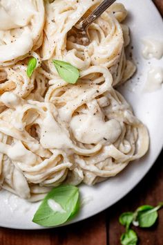 a white plate topped with pasta covered in sauce and garnished with green leaves