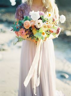 a woman holding a bouquet of flowers in her hand and wearing a dress on the beach