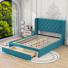 a blue bed with an open drawer underneath it in a white and wood room next to a window