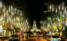 cars driving down a city street with christmas lights on the trees and buildings in the background