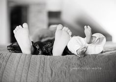 a black and white photo of a baby laying on the bed with his feet up